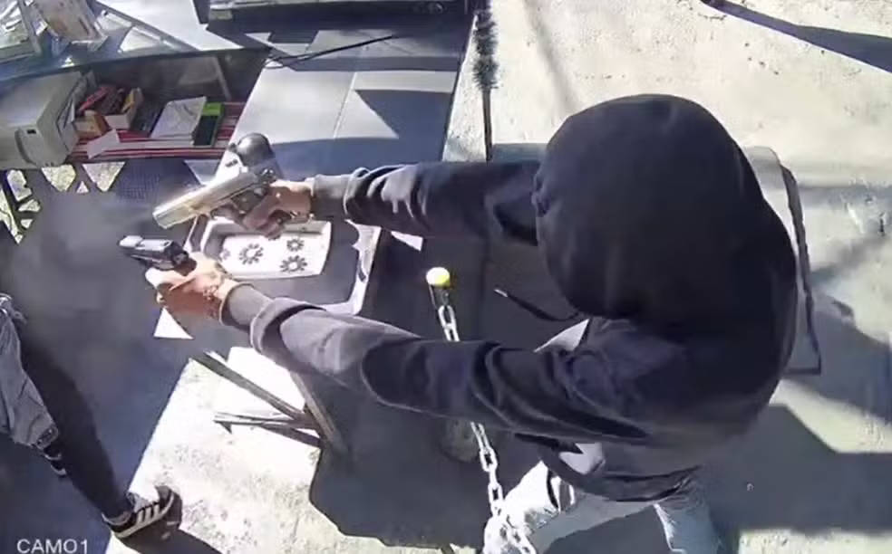 Agressor se aproxima da vítima e pergunta repetidamente: “Você não vai sair?”. Ao ouvir a recusa, ele saca as armas e atira